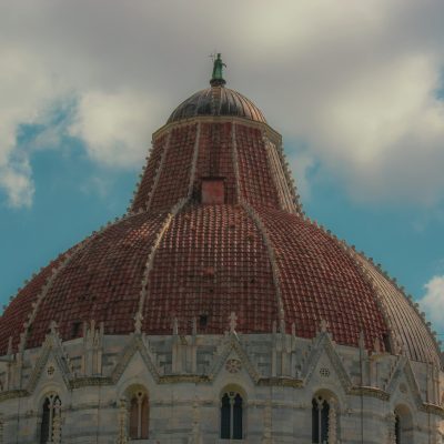 pexels-photo-34049332-34049332 Captivating view of the iconic dome of Pisa Baptistery against a bright blue sky with fluffy clouds.